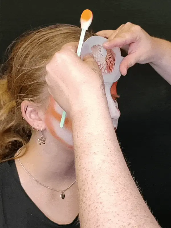 young girl having her face painted white and orange