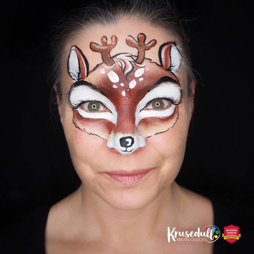 woman looking at the camera with a shaded brown and white reindeer face paint with white spots on her forehead