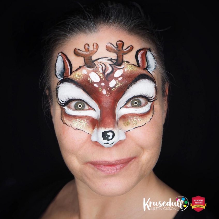 a woman looking at the camera wearing a reindeer face paint design