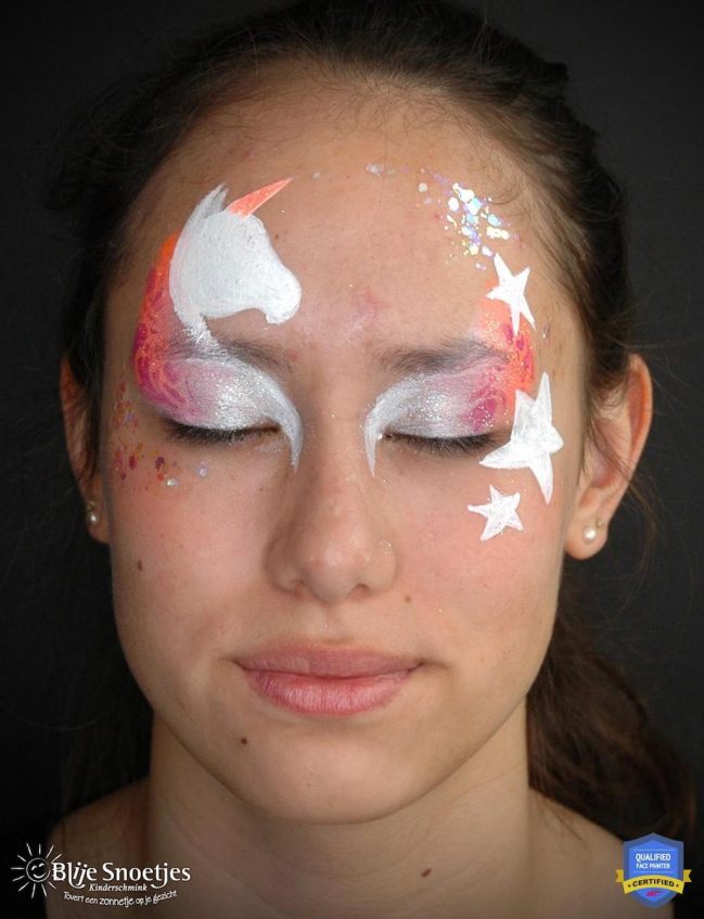 a girl with white eyeshadow with a a base of a unicorn above her right eye and stars around the other eye