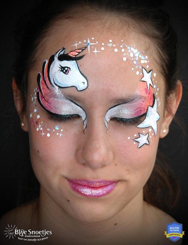 girl with a looking at the camera with a compleated unicorn face paint design above her right eye with white eye shadow