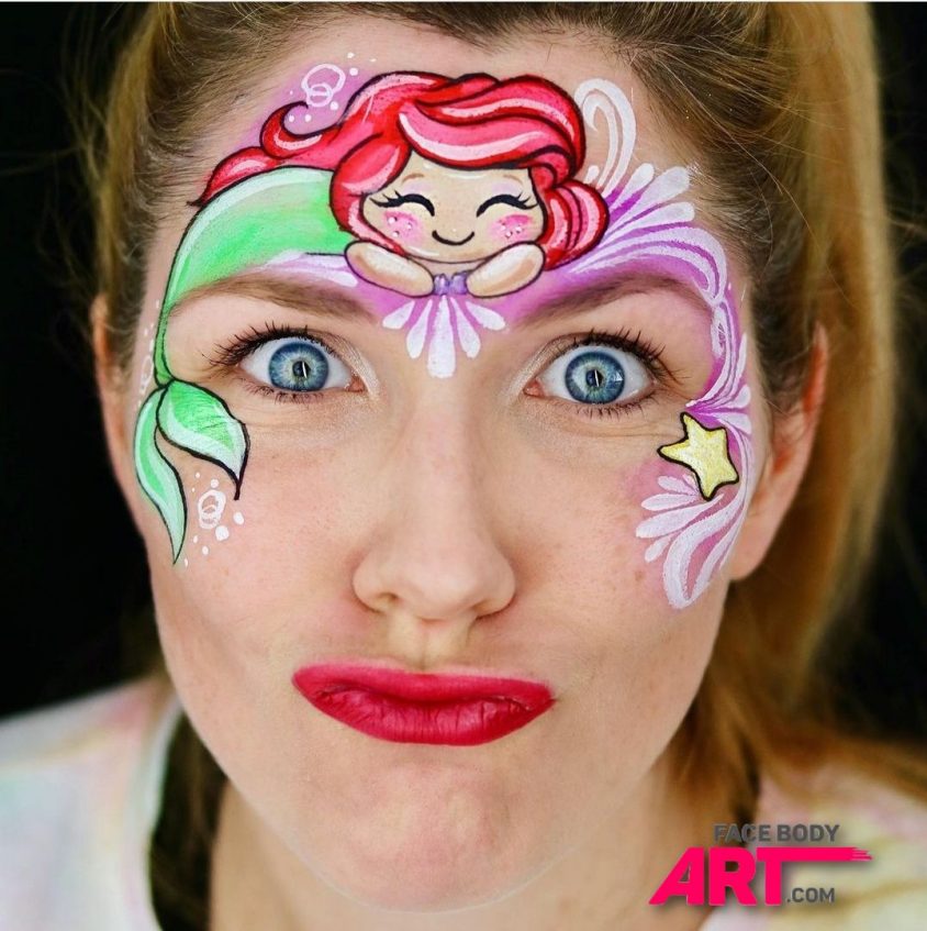 woman looking at the camera making a silly face. she has ariel from the little mermaid painted on her forehead
