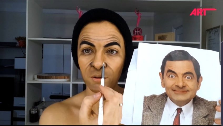 a woman face painting herself to look like mr. bean
